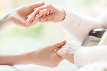 Pflegekraft hält Hände einer Rentnerin