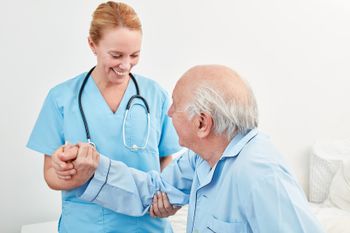 Krankenpflegerin hilft Rentner beim Aufstehen